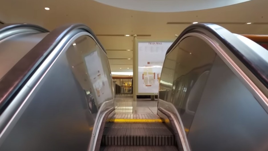 A picture taken while going up an escalator. At the top is the interior map for Fiesta Mall. Way in the background is a closed store.